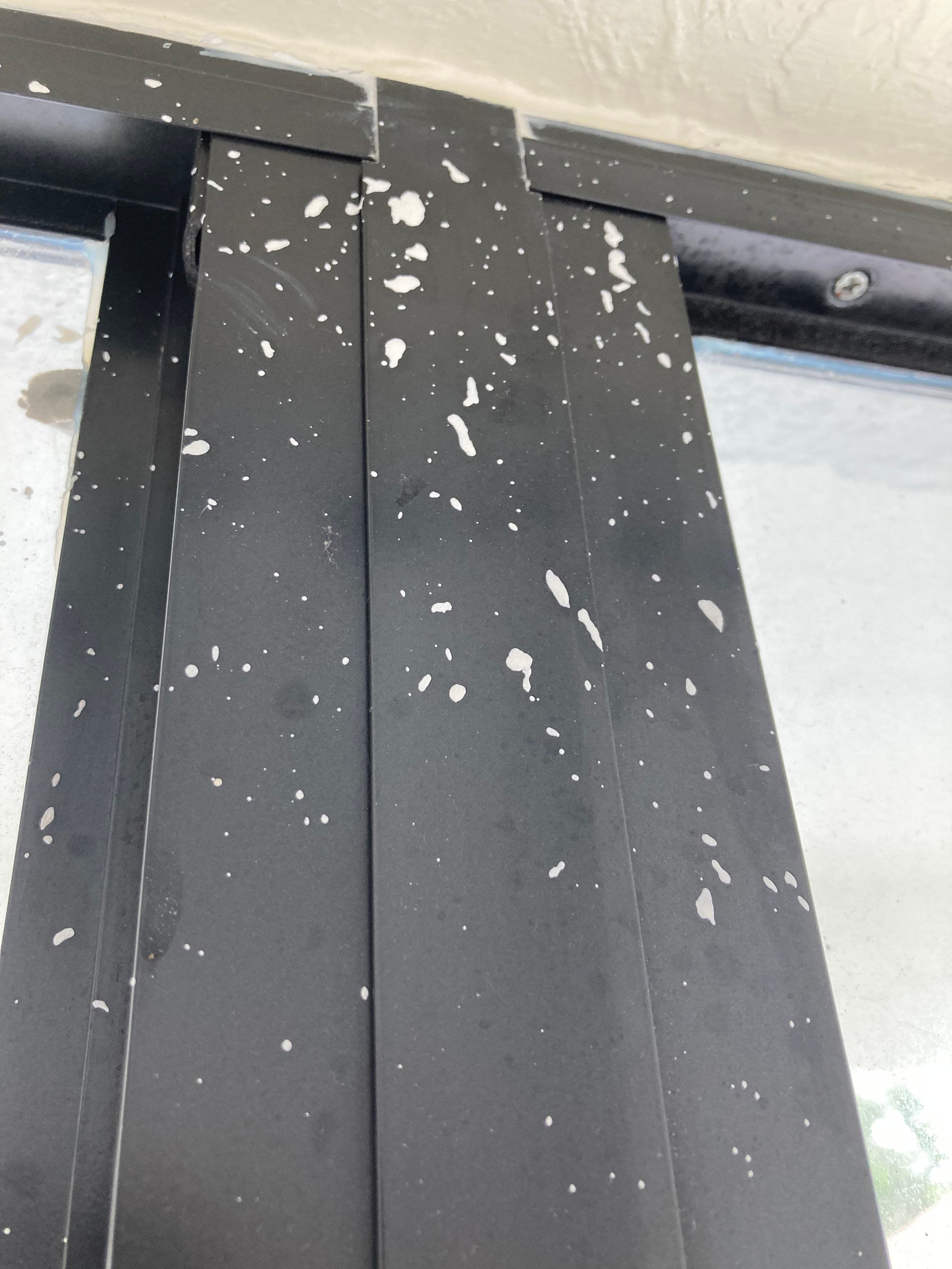 Close-up of black window frame showing white paint splatter and dust particles.