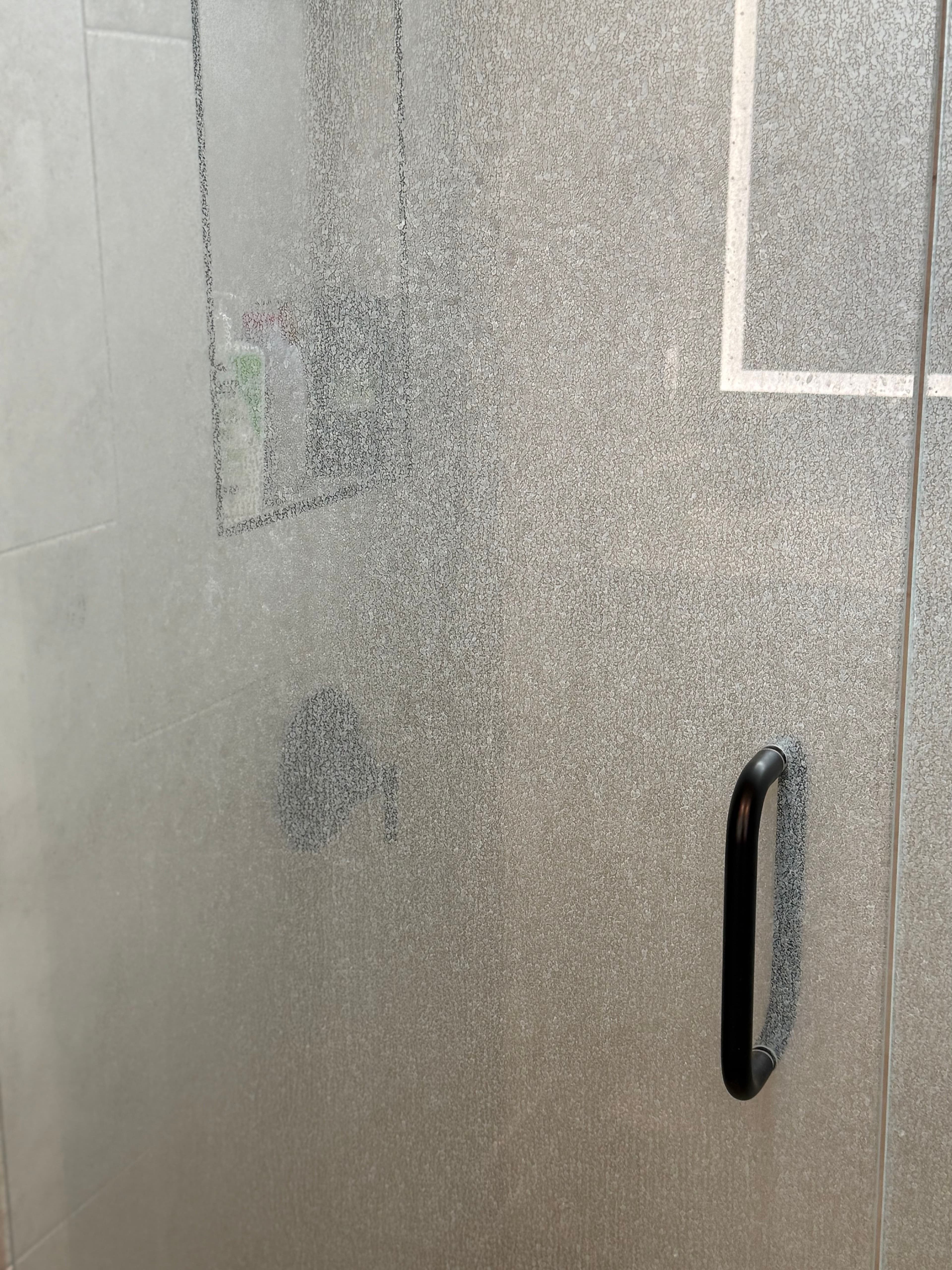 Modern shower enclosure with frosted glass door and black handle in a sleek bathroom setting.