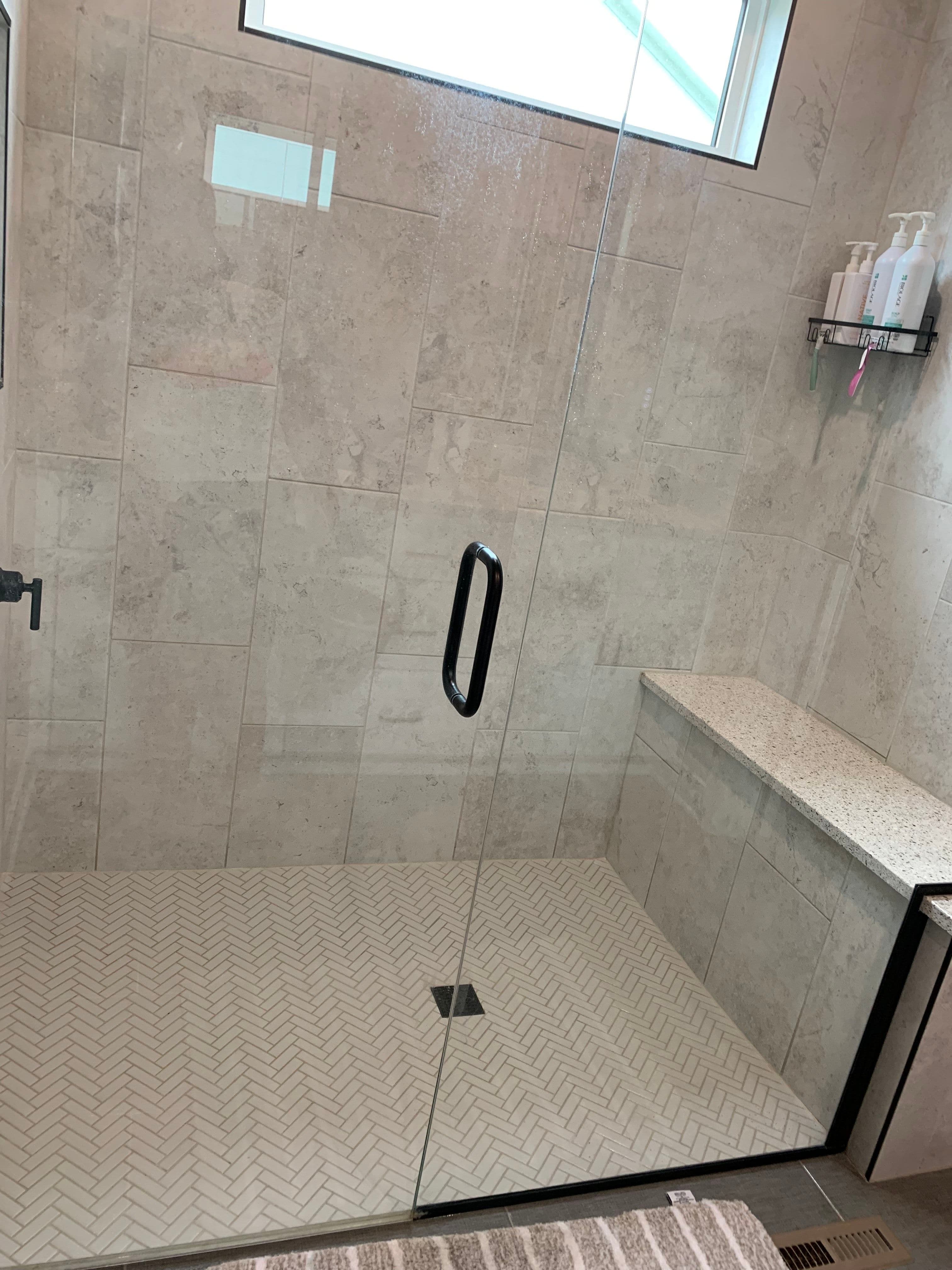 Modern shower design with glass enclosure, herringbone tile flooring, and built-in bench.
